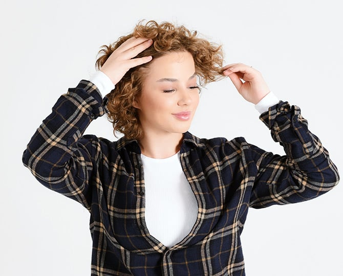 Frau steht seitlich und greift sich in die Haare